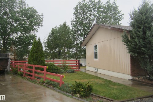 Exterior siding featuring a window, red perimeter fencing, and mature trees - 3814 37 Avenue, Leduc, AB - Outdoor