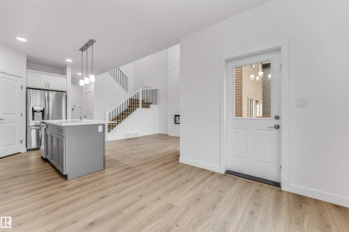 Open-concept living space featuring wood-finish flooring, a two-story ceiling, and a modern staircase with dark metal railings - 1972 210 Street, Edmonton, AB - Indoor Photo Showing Kitchen