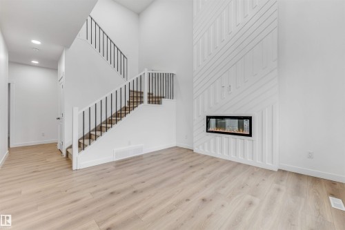 High ceilings complement this open living space featuring wood-finish flooring and a contemporary linear fireplace - 1972 210 Street, Edmonton, AB - Indoor With Fireplace