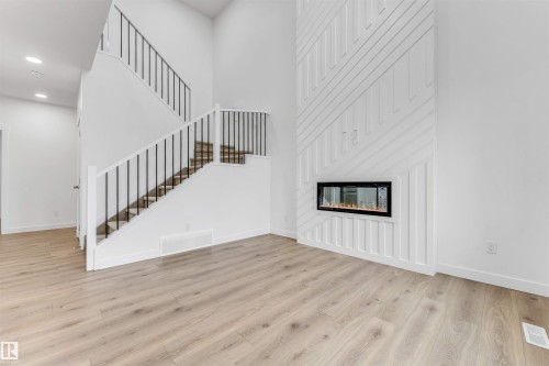 Living area featuring light wood-finish flooring, a contemporary linear fireplace set into a decorative white accent wall, and a staircase with black metal balusters and white risers - 1972 210 Street, Edmonton, AB - Indoor With Fireplace