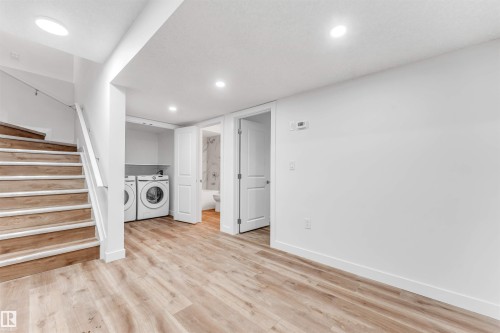 Spacious lower-level area with wood-finish flooring, recessed lighting, and a contemporary white staircase - 1972 210 Street, Edmonton, AB - Indoor Photo Showing Laundry Room