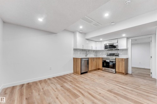 Modern kitchen featuring stainless steel appliances, wood-finish lower cabinetry, white upper cabinetry, and a white marble-patterned backsplash - 1972 210 Street, Edmonton, AB - Indoor Photo Showing Kitchen