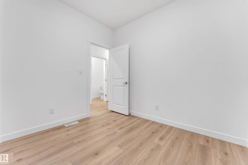 Spacious room featuring light wood-finish flooring, white walls, and a contemporary white interior door - 1972 210 Street, Edmonton, AB - Indoor Photo Showing Other Room