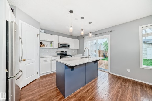 Modern kitchen featuring a central island with a sink, white cabinetry, stainless steel appliances, and wood-finish flooring - 17233 88 Street, Edmonton, AB - Indoor Photo Showing Kitchen With Upgraded Kitchen