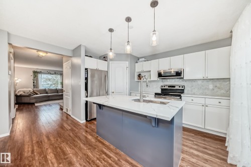 Kitchen featuring a central island with a light-colored countertop and undermount sink, white cabinetry, stainless steel appliances, and wood-finish flooring - 17233 88 Street, Edmonton, AB - Indoor Photo Showing Kitchen With Double Sink With Upgraded Kitchen