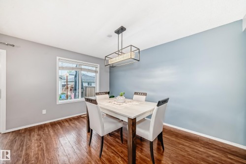 Dining area featuring wood-finish flooring, a contemporary linear chandelier, a large window with blinds, and a contrasting accent wall - 17233 88 Street, Edmonton, AB - Indoor Photo Showing Dining Room