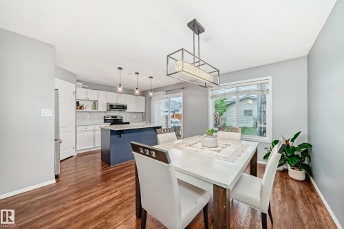 Kitchen and dining area featuring wood-finish flooring, a kitchen island with seating, pendant lighting, white cabinetry, and stainless steel appliances - 17233 88 Street, Edmonton, AB - Indoor Photo Showing Dining Room