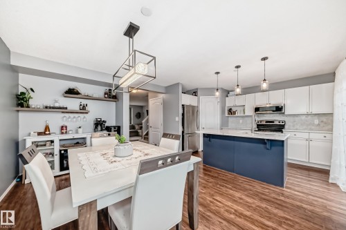 Open-concept kitchen and dining area featuring wood-finish flooring, white cabinetry, a blue kitchen island with a light-colored countertop, and stainless steel appliances - 17233 88 Street, Edmonton, AB - Indoor
