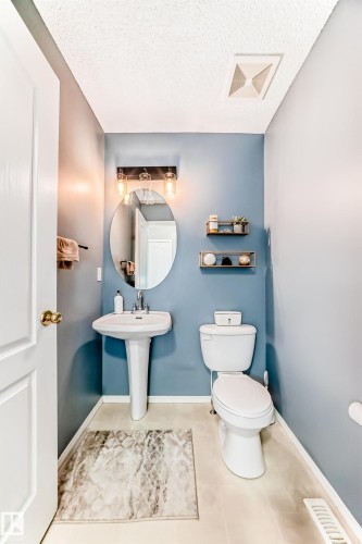 Compact bathroom featuring a pedestal sink, oval vanity mirror, and industrial-style vanity lighting - 17233 88 Street, Edmonton, AB - Indoor Photo Showing Bathroom