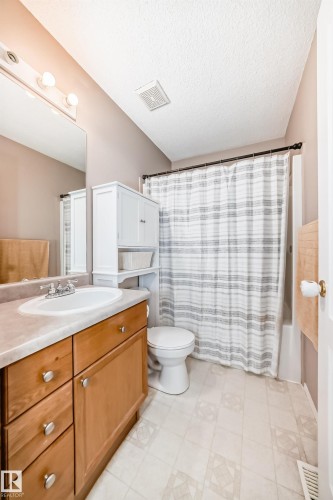 Bathroom featuring a wood-finish vanity with a built-in sink, a wall-mounted mirror, a white toilet, and a combination tub/shower with a shower rod - 17233 88 Street, Edmonton, AB - Indoor Photo Showing Bathroom