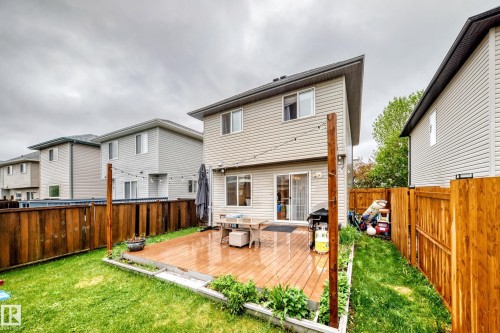 Rear exterior featuring a wooden deck, sliding glass doors, upper-level windows, and a fenced yard with a grassy area - 17233 88 Street, Edmonton, AB - Outdoor With Exterior
