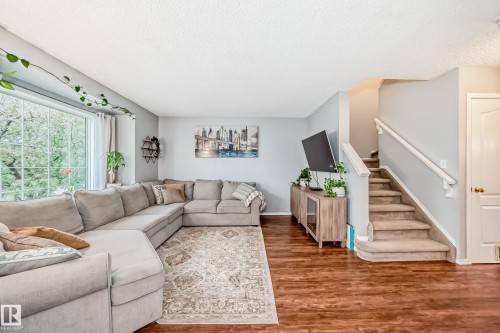 Living area featuring wood-finish flooring, a large picture window, and a carpeted staircase with a white railing - 17233 88 Street, Edmonton, AB - Indoor Photo Showing Living Room