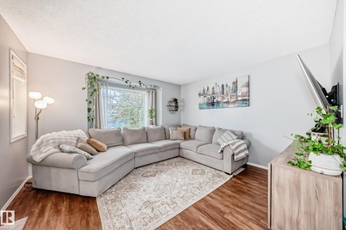 Living area featuring wood-finish flooring, a large window with sheer and opaque drapery, and neutral wall tones - 17233 88 Street, Edmonton, AB - Indoor Photo Showing Living Room