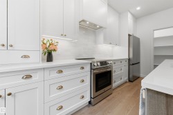 White kitchen featuring shaker-style cabinetry, stainless steel appliances, a subway tile backsplash, light wood-finish flooring, and ample countertop space - 