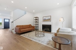 Spacious living area featuring light wood-finish flooring, a contemporary fireplace with a clean surround, and recessed ceiling lights - 