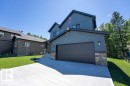 Contemporary residence featuring a two-car garage with a dark panel door, blue siding, and stone accents - 132 Heron Point Close, Rural Wetaskiwin County, AB 