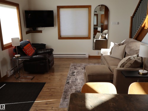 Living area featuring wood-finish flooring, white wall paint, two windows with wood trim, and a built-in wall heater - #20 59316 Rr 54, Rural Barrhead County, AB 