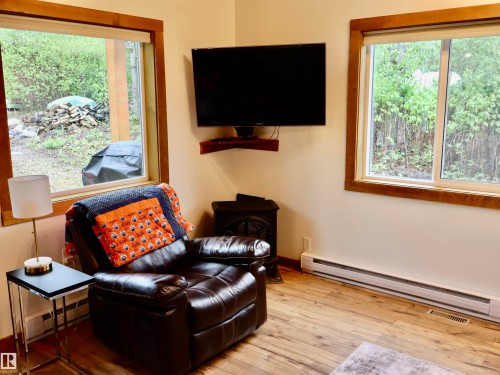 Interior space featuring wood-finish flooring, two window units with wood trim, wall-mounted television, and a corner heating unit - #20 59316 Rr 54, Rural Barrhead County, AB 