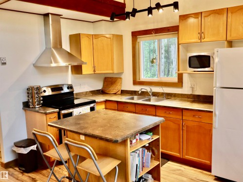 Kitchen featuring warm wood cabinetry, a stainless steel range hood, double basin sink, and a central island with integrated shelving - #20 59316 Rr 54, Rural Barrhead County, AB 