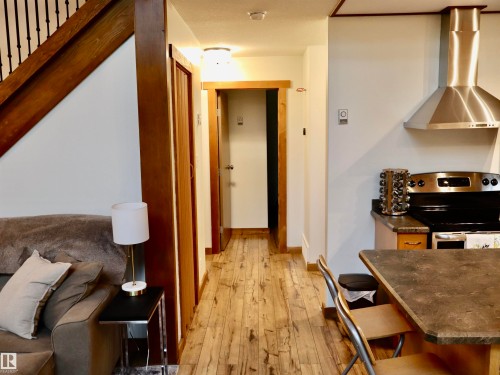 Open-concept area featuring wood-finish flooring, a wood staircase with black iron balusters, a stainless steel range hood, a black range, and a stone-look countertop - #20 59316 Rr 54, Rural Barrhead County, AB 
