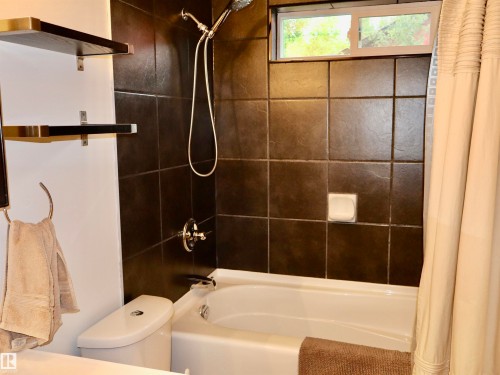 Bathtub with dark tile surround, chrome fixtures, and a white framed transom window - #20 59316 Rr 54, Rural Barrhead County, AB 