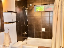 Shower-over-tub combination with dark wall tiling and chrome fixtures - 
