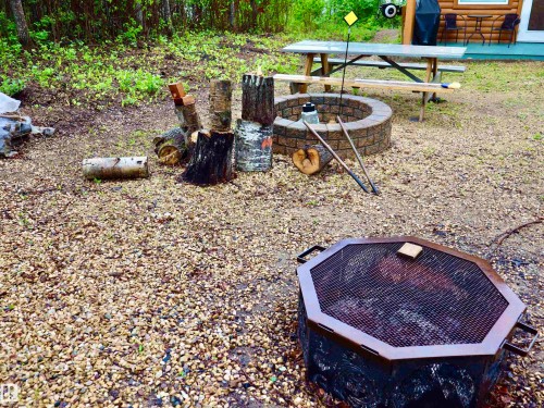 Gravel outdoor area featuring a stone block fire pit, an octagonal metal fire pit, and a picnic table - #20 59316 Rr 54, Rural Barrhead County, AB 