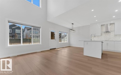 Open-concept living space featuring wood-finish flooring, a contemporary kitchen island with a sink, white cabinetry with integrated appliances, a tiled backsplash, and recessed lighting - 3025 39 Avenue, Beaumont, AB - Indoor Photo Showing Kitchen