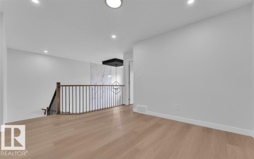 Spacious upper-level landing featuring wood-finish flooring, a dark wood handrail with vertical metal balusters, and a contemporary light fixture - 3025 39 Avenue, Beaumont, AB - Indoor Photo Showing Other Room