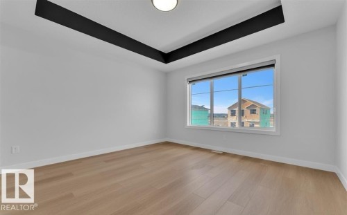 Spacious room featuring wood-finish flooring, a contemporary tray ceiling with a dark accent, and a large window with roller shades - 3025 39 Avenue, Beaumont, AB - Indoor Photo Showing Other Room
