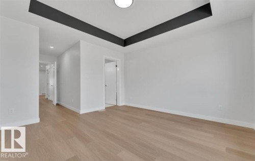Spacious interior room featuring light wood-finish flooring, white walls, and a contemporary ceiling design with dark accent beams and a flush-mount light fixture - 3025 39 Avenue, Beaumont, AB - Indoor Photo Showing Other Room