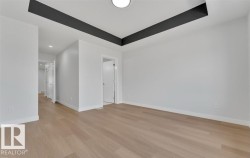 Spacious interior room featuring light wood-finish flooring, white walls, and a contemporary ceiling design with dark accent beams and a flush-mount light fixture - 