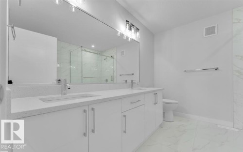 Bathroom featuring a double vanity with white cabinetry and integrated sinks, a large wall-mounted mirror, overhead lighting, and a glass-enclosed shower with marble-look wall tiles - 3025 39 Avenue, Beaumont, AB - Indoor Photo Showing Bathroom