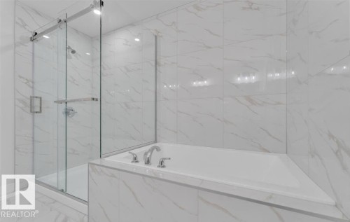 Contemporary bathroom featuring a built-in soaking tub with chrome fixtures, a glass-enclosed shower with a rainfall showerhead, and expansive marble-look tile walls and flooring - 3025 39 Avenue, Beaumont, AB - Indoor Photo Showing Bathroom