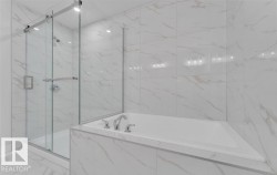 Contemporary bathroom featuring a built-in soaking tub with chrome fixtures, a glass-enclosed shower with a rainfall showerhead, and expansive marble-look tile walls and flooring - 
