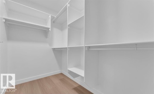 Walk-in closet featuring light wood-finish flooring, white built-in shelving, and multiple clothing rods for organization - 3025 39 Avenue, Beaumont, AB - Indoor With Storage