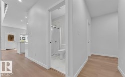 Contemporary interior hallway with wood-finish flooring, recessed lighting, white walls, and a full bathroom featuring a glass-enclosed shower with tiled walls - 