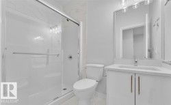 Bathroom featuring a glass-enclosed shower with subway tile surround, white vanity with integrated sink, stone-finish countertop, and a large wall-mounted mirror with overhead lighting - 