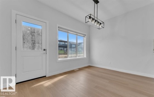 Open concept room featuring wood-finish flooring, a contemporary rectangular light fixture, and large windows with white trim - 3025 39 Avenue, Beaumont, AB - Indoor Photo Showing Other Room