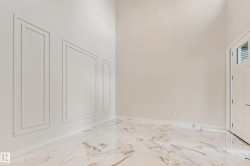 Entryway featuring high ceilings, decorative wall molding, large format marble-look tile flooring, and a white paneled door with louvered glass inserts - 