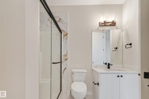 Bathroom featuring a glass-enclosed shower with black trim, a vanity with white cabinetry and a white countertop, a black single-handle faucet, and a wall-mounted light fixture - 4015 39 Street, Beaumont, AB - Indoor Photo Showing Bathroom