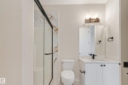 Bathroom featuring a glass-enclosed shower with black trim, a vanity with white cabinetry and a white countertop, a black single-handle faucet, and a wall-mounted light fixture - 