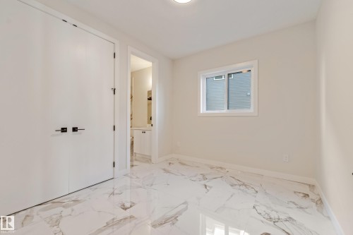 Light-filled room featuring polished marble-look flooring, a window with white trim, and a double-door closet with matte black hardware - 4015 39 Street, Beaumont, AB - Indoor Photo Showing Other Room