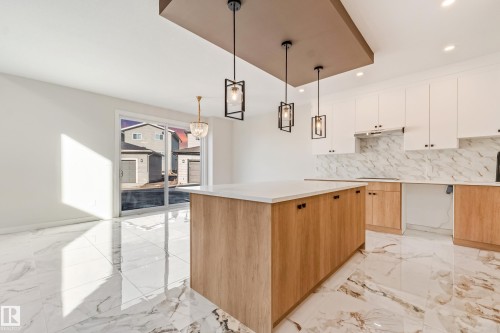 Modern kitchen featuring a central island with wood-finish cabinetry, white countertop, and contemporary pendant lighting - 4015 39 Street, Beaumont, AB - Indoor Photo Showing Kitchen