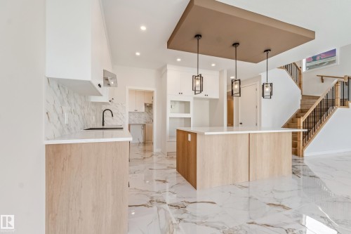 Kitchen featuring an expansive center island with pendant lighting, white upper cabinetry, wood-finish lower cabinetry, and a full-height backsplash - 4015 39 Street, Beaumont, AB - Indoor Photo Showing Kitchen