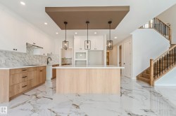 Contemporary kitchen featuring a large central island with a light wood-finish base, white countertop, and three pendant lights - 