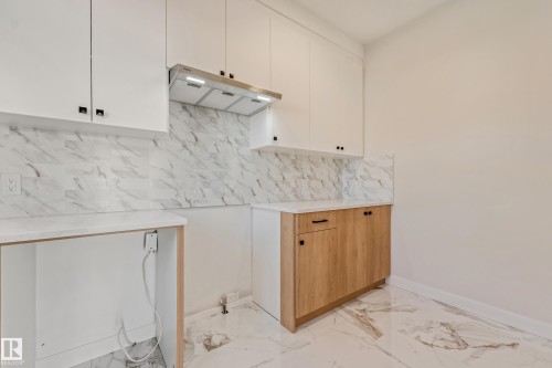 Contemporary kitchen space featuring sleek white upper cabinetry with black hardware, a stainless steel range hood with integrated lighting, and a white and grey veined backsplash - 4015 39 Street, Beaumont, AB - Indoor
