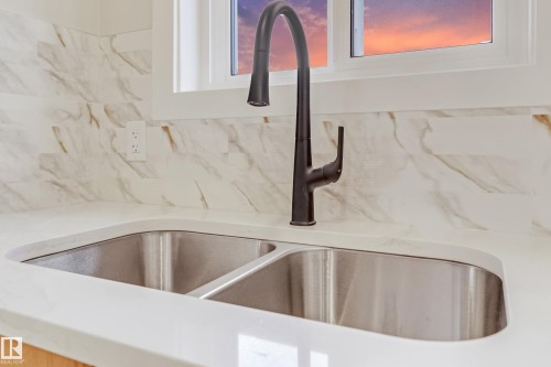 Dual basin stainless steel sink with a matte black gooseneck faucet, set within a white countertop - 4015 39 Street, Beaumont, AB - Indoor Photo Showing Kitchen With Double Sink