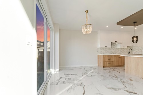 Spacious interior featuring large format tile flooring, a modern kitchen with two-tone cabinetry, a stone backsplash, and an island with an undermount sink - 4015 39 Street, Beaumont, AB - Indoor Photo Showing Kitchen