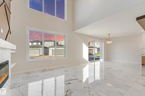 Two-story living area featuring high ceilings, large windows, an integrated fireplace with a marble-finish surround, and polished marble-finish flooring - 4015 39 Street, Beaumont, AB - Indoor Photo Showing Other Room With Fireplace